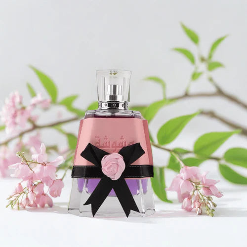 Perfume bottle with pink rose and black bow against a light background with green leaves and pink flowers.