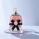 Perfume bottle with pink label and black bow on a light blue background